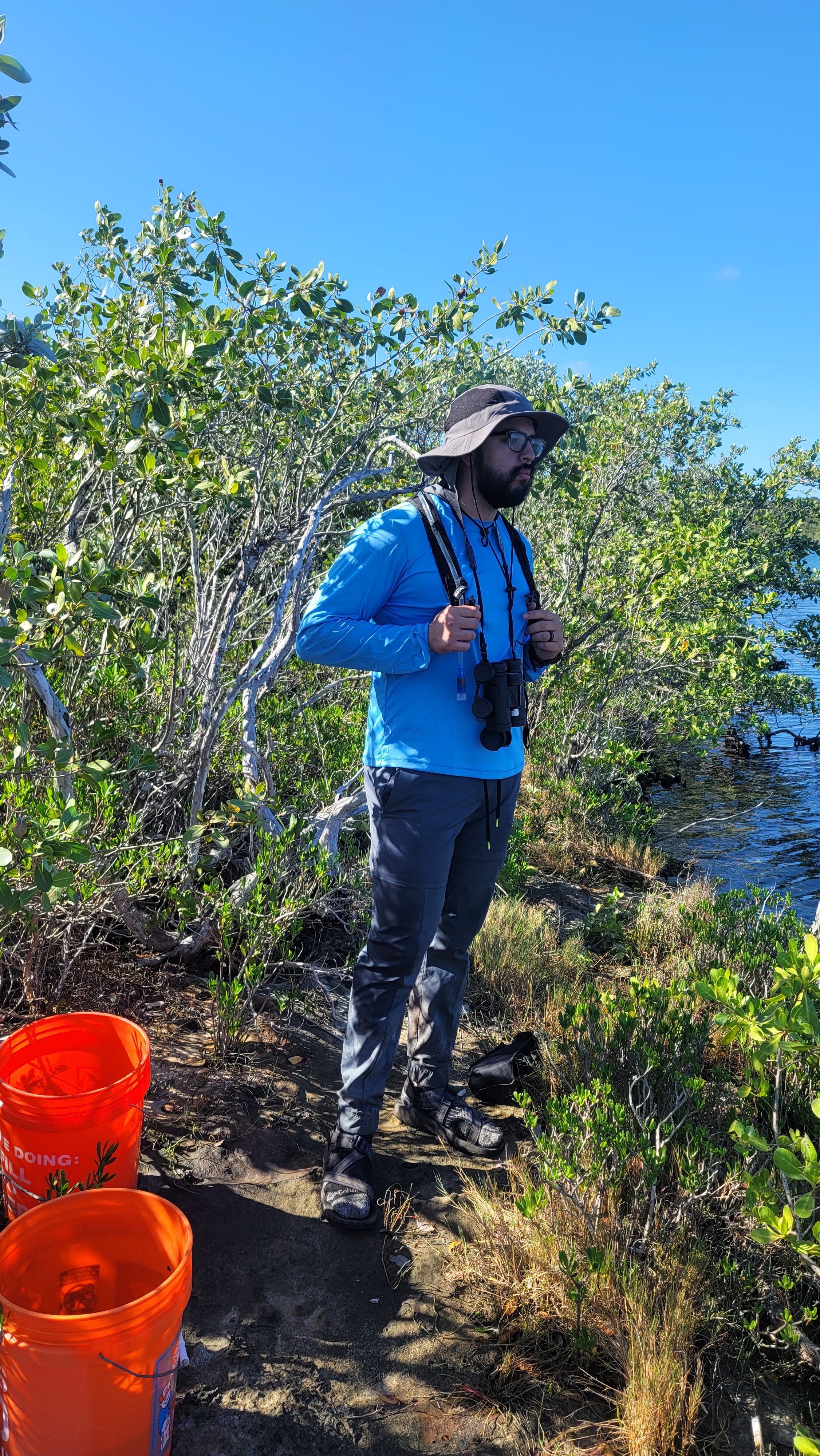 Vincent Benavidez stands in a mangrove swamp with two orange buckets for collecting fish.